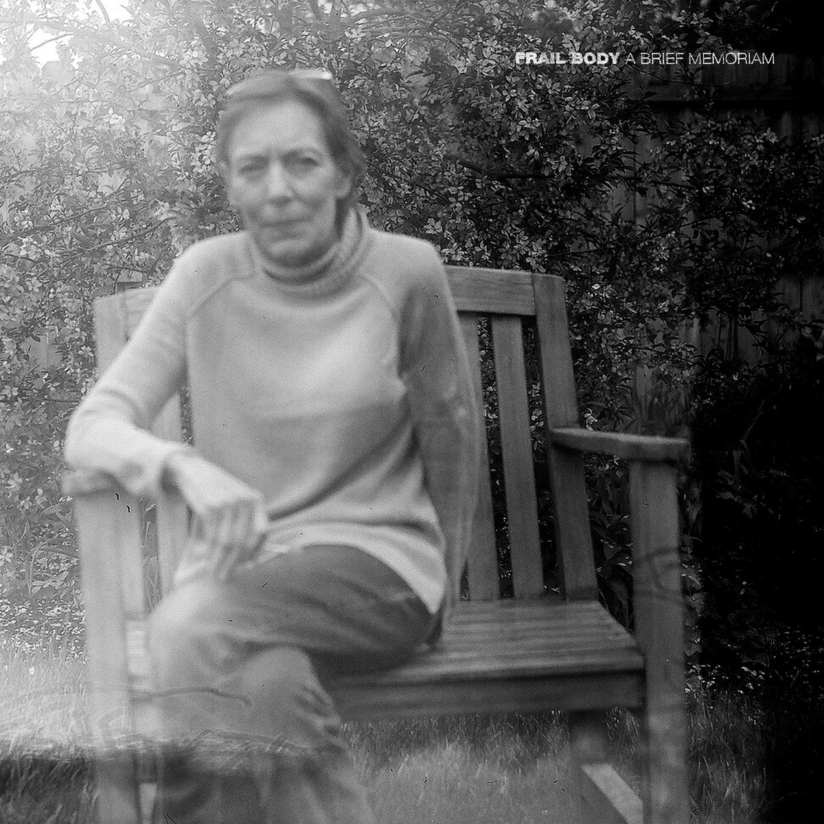 An album cover of Frail body’s first album A Brief Memoriam, featuring a black and white photo of an older woman sitting on a wooden chair in front of a wood fence and branches.